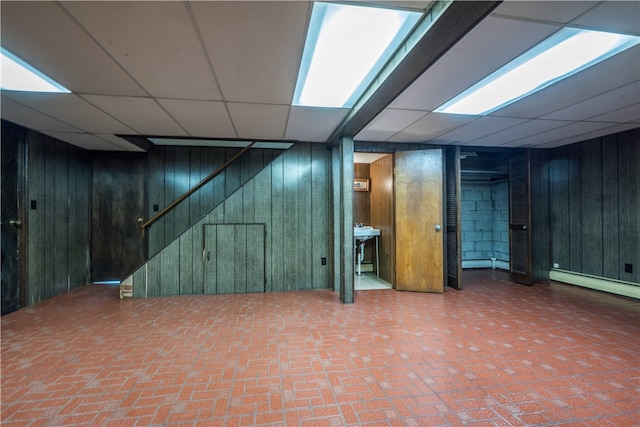 basement featuring wood walls and a paneled ceiling