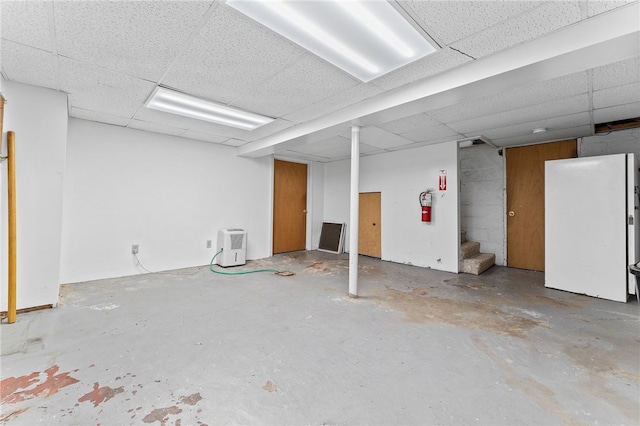 basement featuring a drop ceiling and white refrigerator