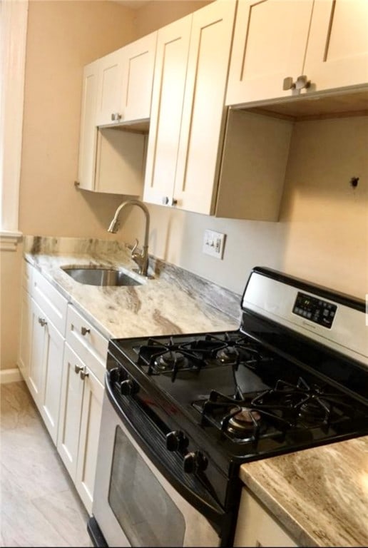 kitchen featuring white cabinetry, sink, light stone counters, and gas stove