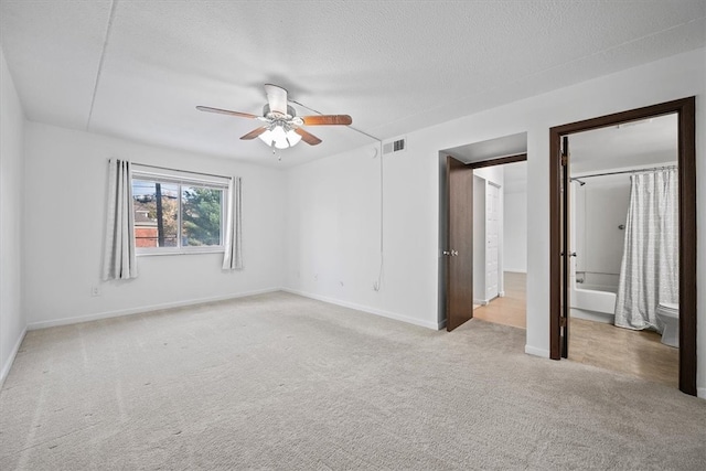 unfurnished bedroom featuring ensuite bathroom, ceiling fan, a textured ceiling, and light colored carpet