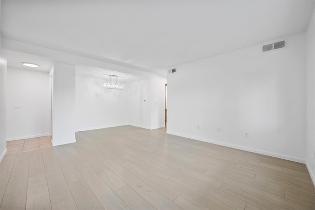 empty room featuring a notable chandelier and light hardwood / wood-style flooring