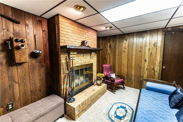 living room featuring a fireplace, wood walls, a paneled ceiling, and carpet flooring