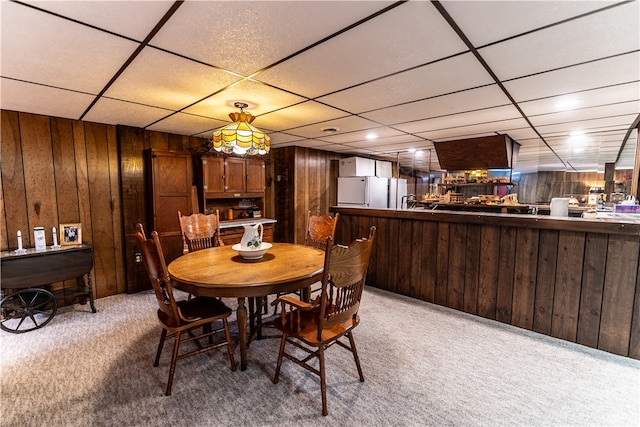 dining space featuring a drop ceiling, wooden walls, and light carpet