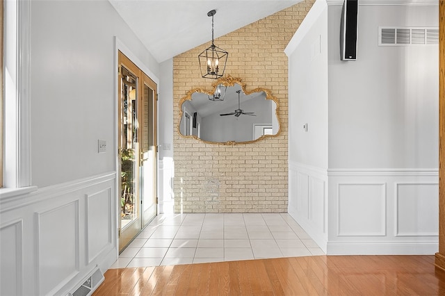 tiled foyer entrance featuring ceiling fan with notable chandelier, brick wall, and lofted ceiling