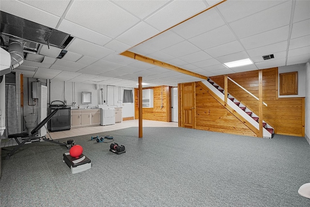 exercise area with a drop ceiling, wood walls, and independent washer and dryer