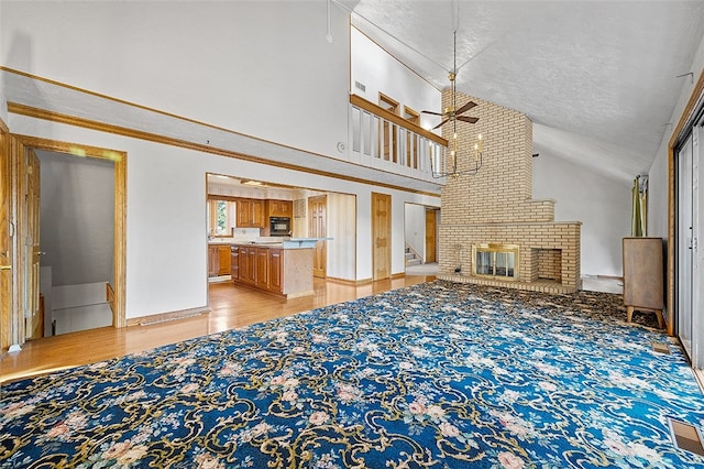 unfurnished living room with light wood-type flooring, a textured ceiling, high vaulted ceiling, a brick fireplace, and ceiling fan