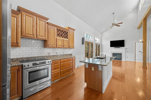 kitchen featuring sink, dark stone countertops, high vaulted ceiling, an island with sink, and stainless steel range