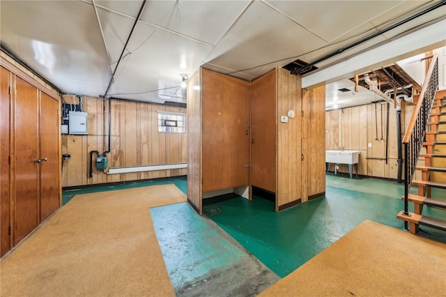 basement featuring electric panel, wood walls, and a baseboard radiator