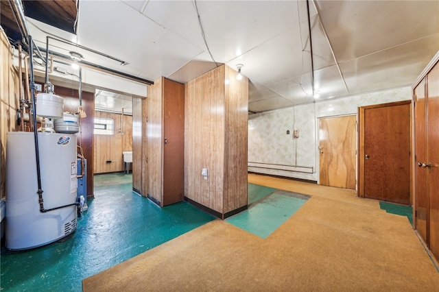 basement featuring baseboard heating, wooden walls, and gas water heater