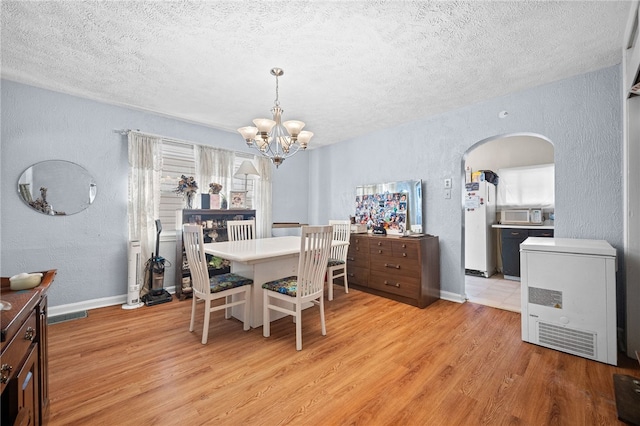 dining room with light hardwood / wood-style floors, a textured ceiling, and a notable chandelier