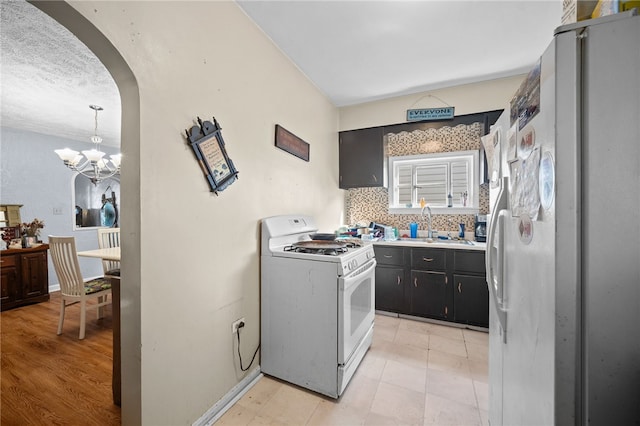 kitchen with a notable chandelier, sink, tasteful backsplash, light hardwood / wood-style flooring, and white appliances