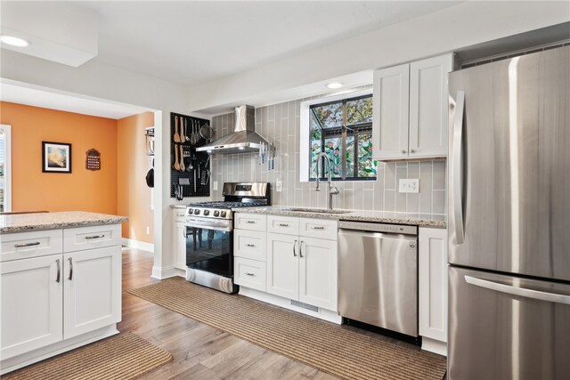 kitchen featuring wall chimney exhaust hood, white cabinetry, sink, and appliances with stainless steel finishes