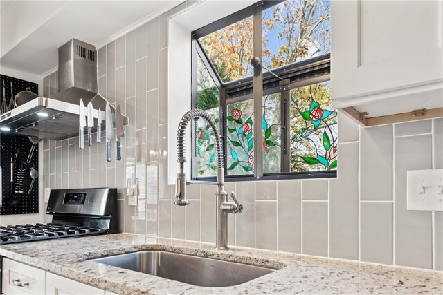 kitchen with white cabinetry, sink, light stone countertops, wall chimney exhaust hood, and stainless steel range oven