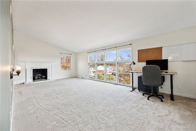 office space with a high end fireplace, light colored carpet, and vaulted ceiling