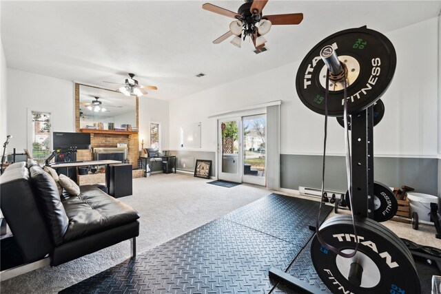 exercise room with a brick fireplace, carpet floors, and ceiling fan