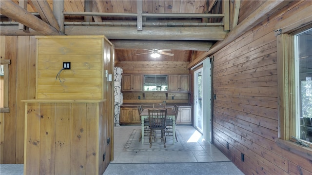 unfurnished dining area featuring lofted ceiling with beams, wood walls, light tile patterned floors, and ceiling fan