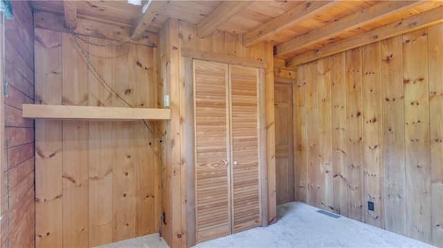 unfurnished bedroom featuring a closet, carpet floors, wood walls, beamed ceiling, and wooden ceiling