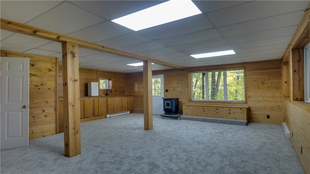 basement with wood walls, a drop ceiling, a wood stove, light colored carpet, and a baseboard radiator