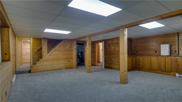 basement with a drop ceiling, light colored carpet, and wood walls