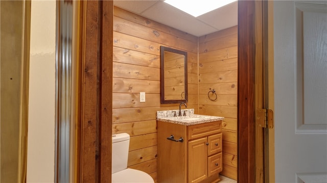 bathroom with toilet, wood walls, and vanity