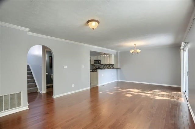 unfurnished living room with an inviting chandelier, dark hardwood / wood-style floors, and crown molding