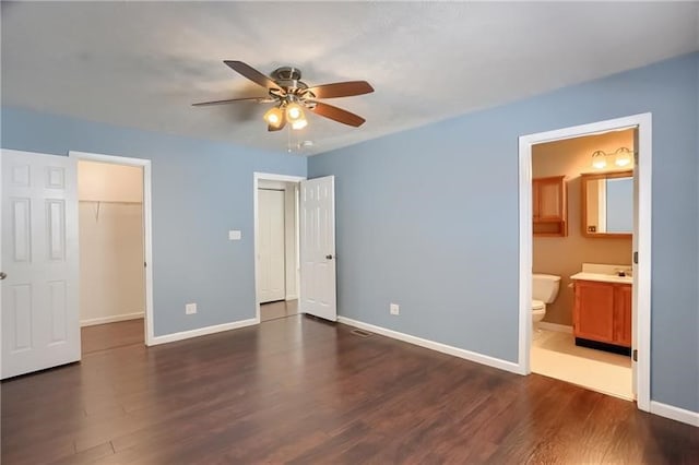 unfurnished bedroom featuring a closet, a spacious closet, connected bathroom, dark hardwood / wood-style flooring, and ceiling fan