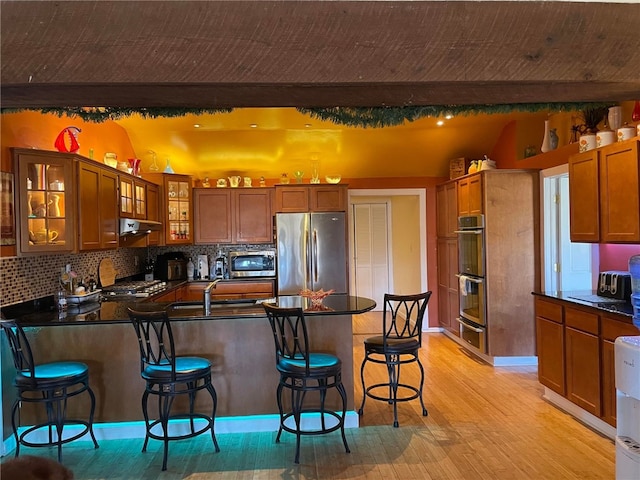 kitchen with backsplash, light wood-type flooring, appliances with stainless steel finishes, a kitchen bar, and kitchen peninsula