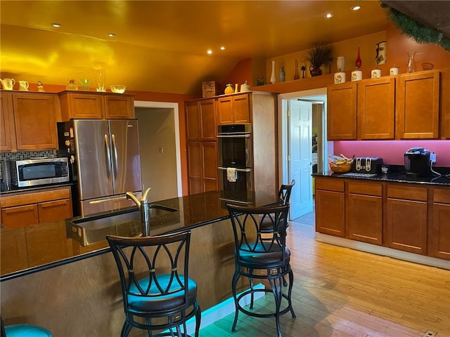 kitchen featuring stainless steel appliances, dark stone counters, a kitchen bar, vaulted ceiling, and light hardwood / wood-style floors