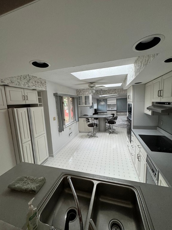 kitchen featuring black electric stovetop, sink, dishwasher, a skylight, and ceiling fan