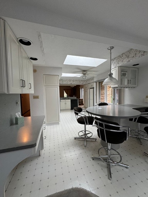 kitchen with white cabinetry, a skylight, hanging light fixtures, kitchen peninsula, and ceiling fan