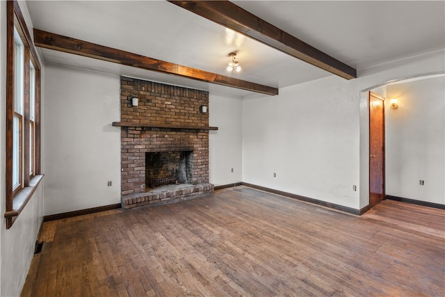 unfurnished living room featuring a brick fireplace, hardwood / wood-style flooring, and beam ceiling