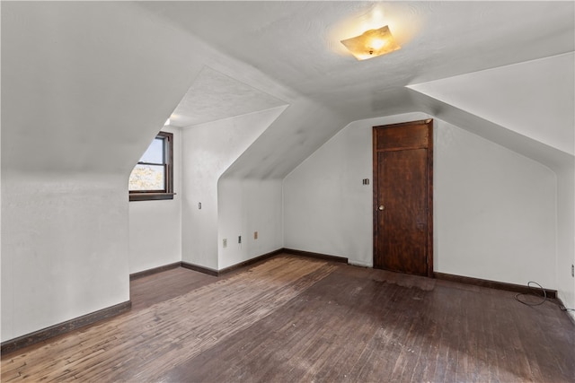 additional living space with dark wood-type flooring, vaulted ceiling, and a textured ceiling