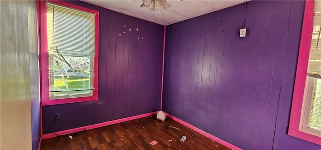 unfurnished room with hardwood / wood-style flooring, a healthy amount of sunlight, wooden walls, and ceiling fan