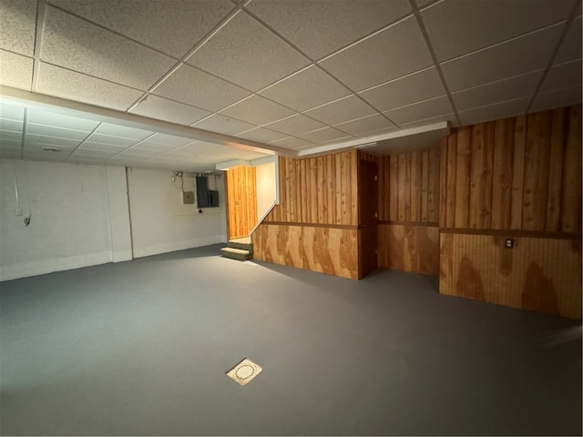 basement featuring a drop ceiling and wood walls