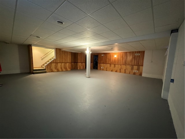 basement with a drop ceiling and wood walls