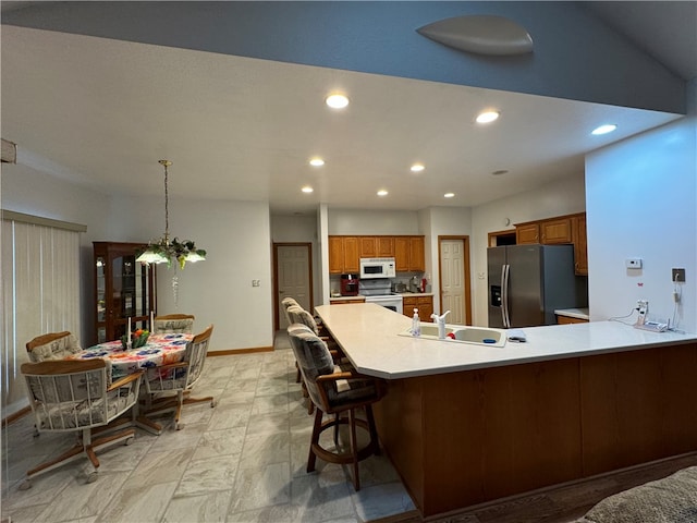 kitchen featuring sink, hanging light fixtures, electric range, stainless steel fridge, and a breakfast bar area