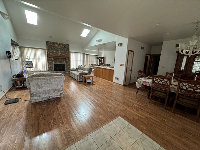 living room with a brick fireplace, lofted ceiling with skylight, and light wood-type flooring