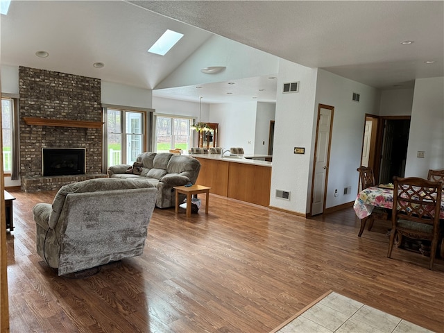 living room with a skylight, wood-type flooring, high vaulted ceiling, a fireplace, and a chandelier