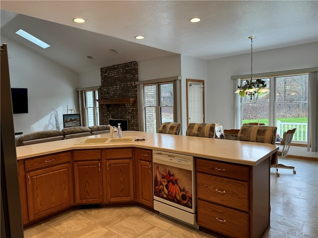 kitchen with a fireplace, white dishwasher, a healthy amount of sunlight, and vaulted ceiling with skylight