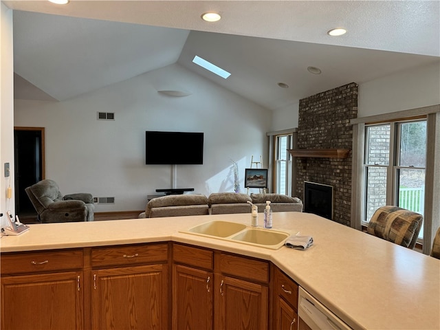 kitchen with sink, a brick fireplace, a healthy amount of sunlight, and vaulted ceiling with skylight