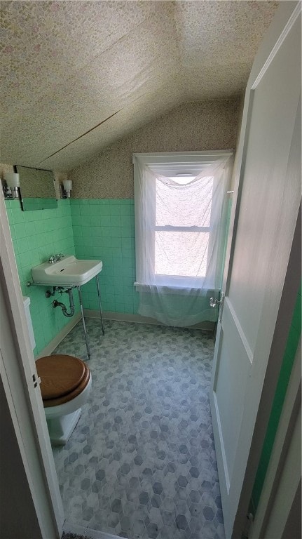 bathroom featuring sink, a textured ceiling, lofted ceiling, toilet, and tile walls