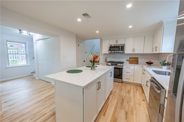 kitchen featuring light hardwood / wood-style floors, white cabinets, a kitchen island, backsplash, and appliances with stainless steel finishes