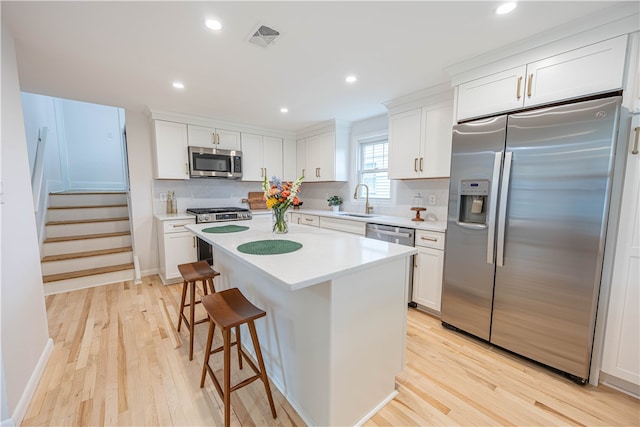 kitchen featuring stainless steel appliances, sink, light hardwood / wood-style flooring, a kitchen island, and white cabinets