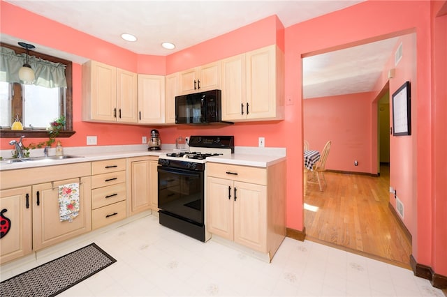 kitchen featuring hanging light fixtures, sink, black appliances, and light hardwood / wood-style flooring