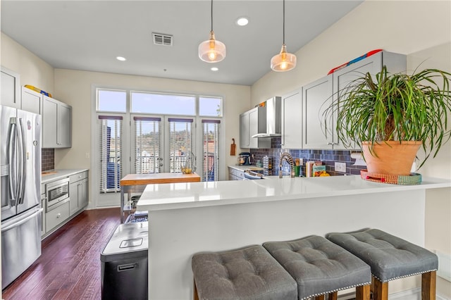 kitchen featuring a kitchen bar, stainless steel appliances, dark wood-type flooring, kitchen peninsula, and backsplash