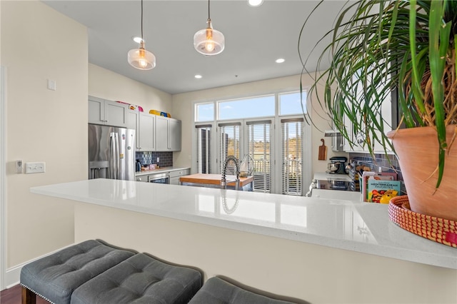 kitchen featuring kitchen peninsula, tasteful backsplash, stainless steel refrigerator with ice dispenser, gray cabinetry, and pendant lighting