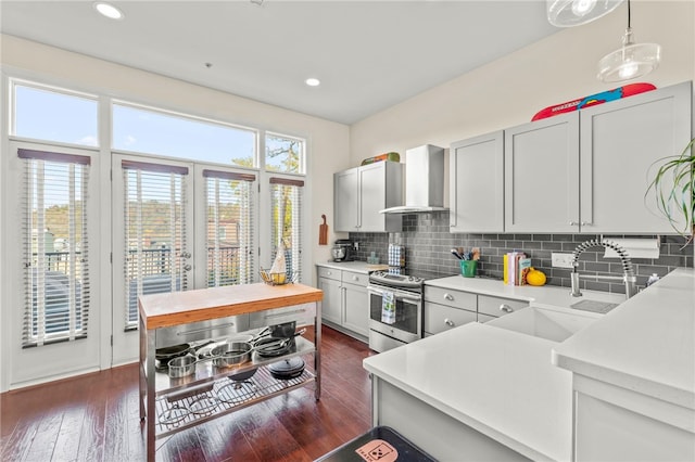 kitchen featuring wall chimney exhaust hood, stainless steel range with electric cooktop, dark hardwood / wood-style flooring, pendant lighting, and decorative backsplash