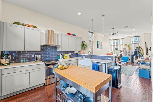 kitchen featuring sink, appliances with stainless steel finishes, wall chimney exhaust hood, pendant lighting, and dark hardwood / wood-style flooring