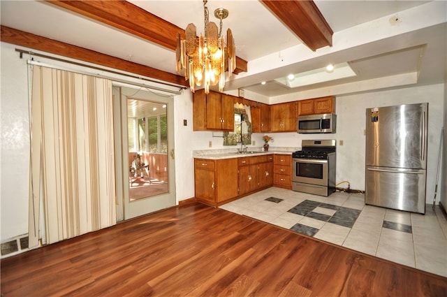 kitchen featuring light wood-type flooring, decorative light fixtures, beam ceiling, and stainless steel appliances