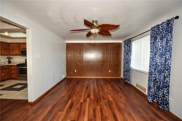 empty room with dark wood-type flooring, wood walls, and ceiling fan